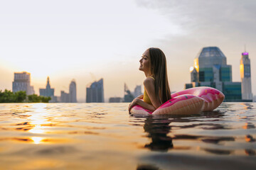 Black silhouette of asian woman splash water on summer vacation holiday relaxing in infinity swimming pool with blue sea sunset view. Healthy happiness lifestyle