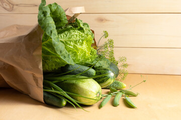 Close-up shot of fresh natural green vegetables, chinese cabbage, cucumbers, zucchini, peas in craft paper bag on wooden background