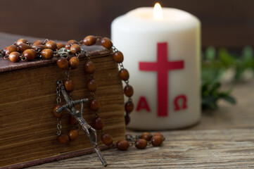 Wooden cross with bible, rosary and paschal candle, easter religious concept 