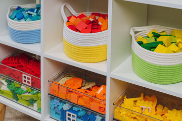 Colorful storage baskets and transparent plastic boxes on shelves. White shelving with rainbow colored toys in cloth stylish baskets. Toys sorting system. Organizing and Storage Ideas in playroom.