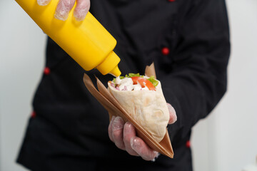 Chef cook pouring white tzatziki sauce on pita crete snack in fast food restaurant. Traditional...