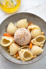 Close-up of escudella soup with pasta, chickpeas and pilota served in a grey plate, vertical shot, selective focus