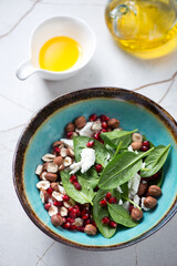 Turquoise bowl with spinach, pomegranate, goat cheese and hazelnuts salad, vertical shot on a beige marble background, elevated view