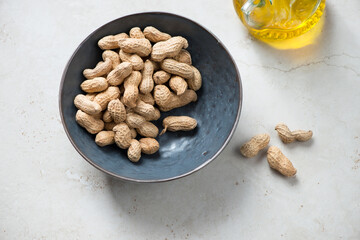 Dark-grey bowl with peanuts on a light-beige stone background, horizontal shot