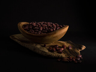 Red beans in a wooden plate on a black background.