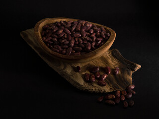 Red beans in a wooden plate on a black background.