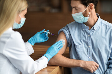 Doctor Woman Making Vaccination Shot To Male Patient Wearing Medical Mask