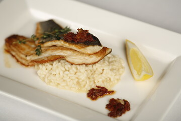 White grilled fish dish with white rice and sun dried tomatoes and slice of a lemon. Fancy low calorie meal in restaurant quality and white dish 