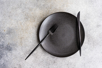 Minimalistic table on a concrete background with a plate a knife and a fork