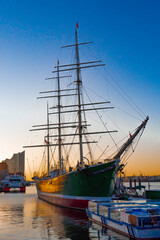 Fototapeta na wymiar Blick von Nordwesten auf ein Museumsschiff in Hamburg während des Sonnenaufgangs, Ausflugsschiffe und die Elbphilharmonie mit im Bild, vertikal 