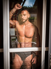 Portrait of sexy shirtless muscular man next to window