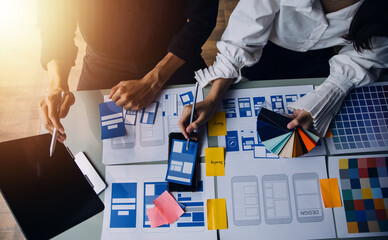 Close up ux developer and ui designer brainstorming about mobile app interface wireframe design on table with customer breif and color code at modern office.Creative digital development agency