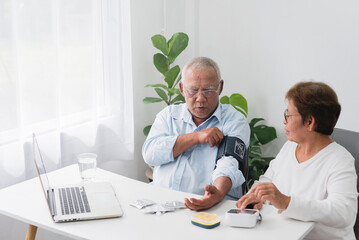 Asian senior men and women Using blood pressure monitor, on doctor's advice through laptop. At home, telemedicine concept. - obrazy, fototapety, plakaty