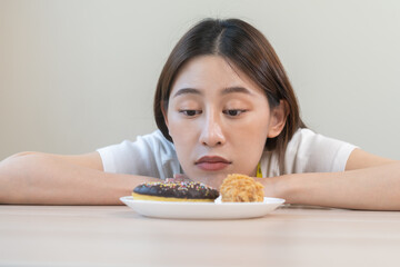 Diet, dieting asian young woman, girl expression face bored, looking at doughnut, bakery and fried chicken, fast food in plate to loss weight. Passion, temptation when hungry restrained to eat.