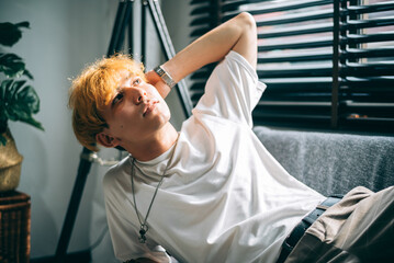 Portrait of caucasian hipster young man fashionable blonde hair sitting in living room.