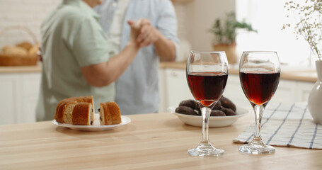 Sweet mature asian couple relaxing in kitchen, listening to music, drinking wine and cutely dancing, enjoying their retirement - senior lifestyle, anniversary concept 