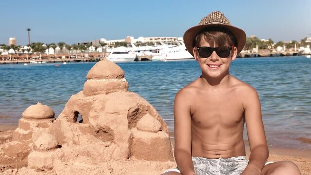 Tanned male kid posing at sand castle beach sea sunny coastline landscape summer travel vacation