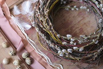 A fragment of an Easter wreath made of tree branches and a pussy willow on a wooden background with decorative elements for Easter: quail eggs, feathers, silk ribbons, decorative braid of sequins  © Valerie