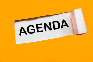 Business and agenda symbol. The concept of Agenda appears behind torn white paper. Beautiful yellow background, copy space. Business and agenda concept.