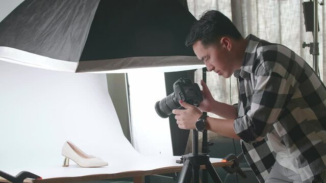 Asian Male Photographer Walking Into Home Studio To Adjust Position Of Women'S Shoes Before Taking Photos Of Them
