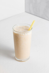 Milkshake with banana in a high transparent glass on a white background. A healthy drink for a diet