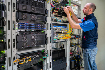 A man commutes wires in a server room. A technician works with server equipment in a data center.