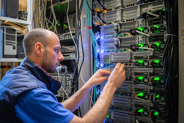 A technician works with server equipment in a data center. A man commutes wires in a server room.
