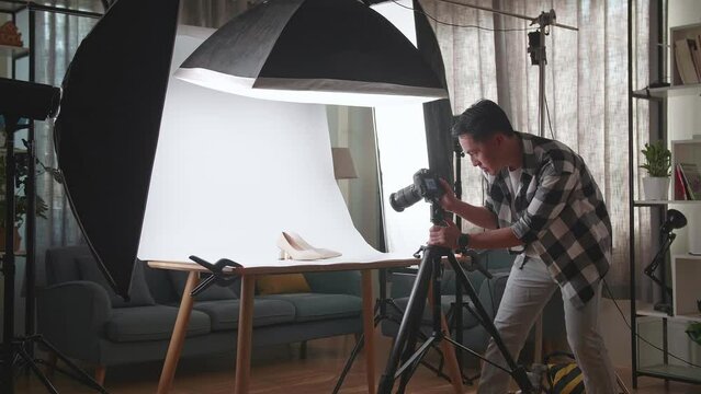 Asian Male Photographer Thinking About Women'S Shoes Position Then Raising His Index Finger While Taking Photos Of Them In Home Studio 
