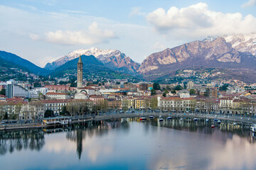 Fototapeta na wymiar Cloudy aerial cityscape of Lecco town on spring evening. Picturesque waterfront of Lecco town located between famous Lake Como and scenic Bergamo Alps mountains.
