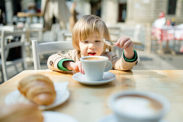 Cute toddler boy having hot chocolate in outdoor cafe. Small child drinking hot beverage on sunny...