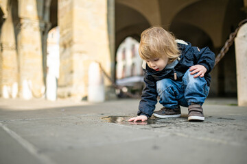Cute toddler boy playing in a puddle on the street of Bergamo. Little child having fun exploring in Citta Alta, upper district of Bergamo. Bergamo, Italy.