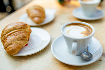 Two cups of capuccino coffee with croissants on a wooden table.