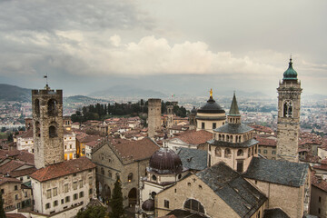 Fototapeta na wymiar Scenic aerial view of Bergamo city northeast of Milan, on cloudy evening. Flying over Citta Alta, town's upper district encircled by Venetian walls. Bergamo, Italy.