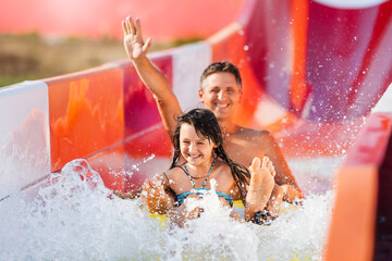 Happy family rushes down high slide on an inflatable circle in water park. Father and daughter in...
