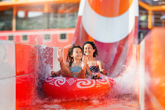 Happy family rushes down high slide on an inflatable circle in water park.