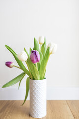 Fresh pink tulip bouquet on a shelf in front of a white wall. View with copy space