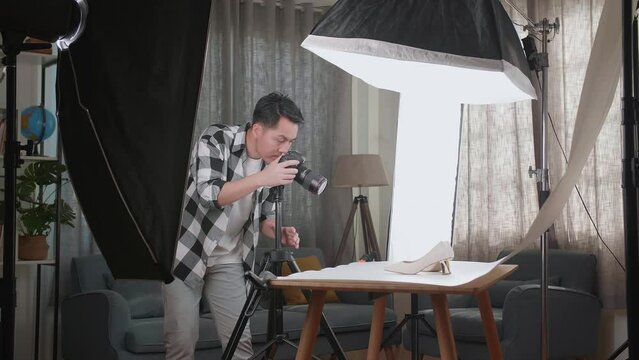 Asian Male Photographer Thinking And Adjusting Position Of Women'S Shoes While Taking Photos Of Them In Home Studio 

