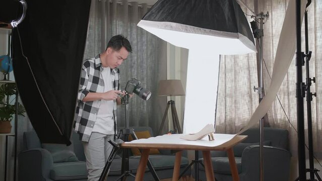 Asian Male Photographer Talking On Smartphone While Taking Photos Of Women'S Shoes In Home Studio 
