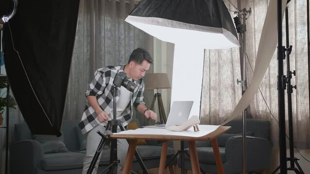 Asian Male Photographer Comparing Photos On A Laptop To Camera While Taking Photos Of Women'S Shoes In Home Studio 
