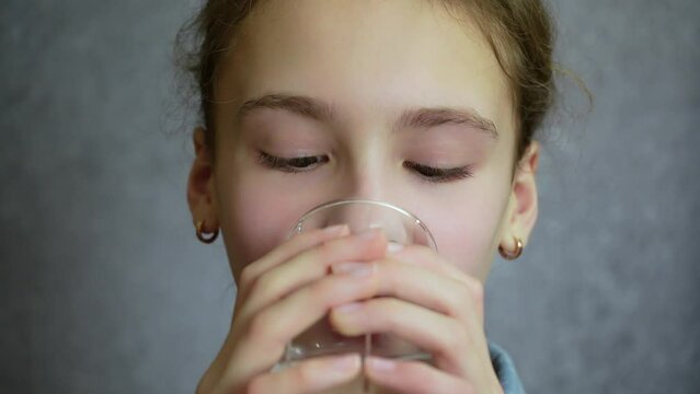 Cute 12 years old girl drinks water from clear glass. Slow motion
