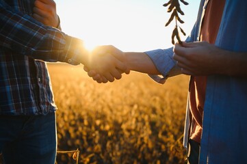 Two farmers shaking hands in soybean field. - obrazy, fototapety, plakaty