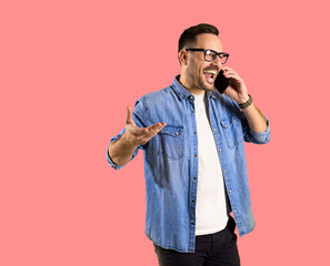 Handsome mid adult man dressed in denim jacket gesturing and screaming excitedly while talking over smartphone isolated on pink background