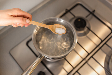 The girl is adding salt to boiling water, seasoning the dish she's cooking