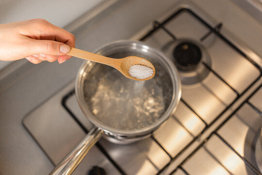 The Girl Is Adding Salt To Boiling Water, Seasoning The Dish She's Cooking