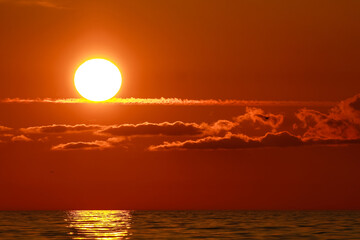 Sun setting with red orange skies and few clouds over the Baltics sea