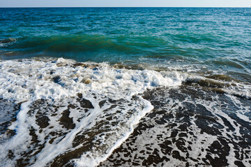 Floating foamy waves roll onto the sea or ocean shore. The water is turquoise