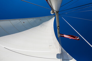 White sails with national flag of Republic of Latvia in the wind on a sailboat