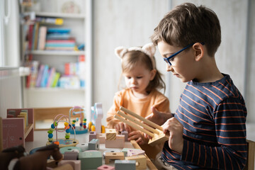 Fototapeta premium Two children brother and sister sitting and playing at home with wooden toys in playroom, modern family, early child development, learning and play concept
