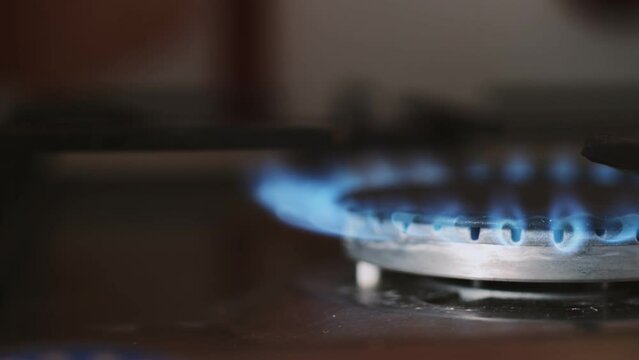 Gas-ring on a home kitchen stove starts burning close up. Using home gas cooking equipment. Tongues of blue and red flames escape from under the gas burner