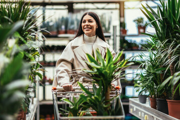 Woman buying flowers pushing shopping cart in garden center.